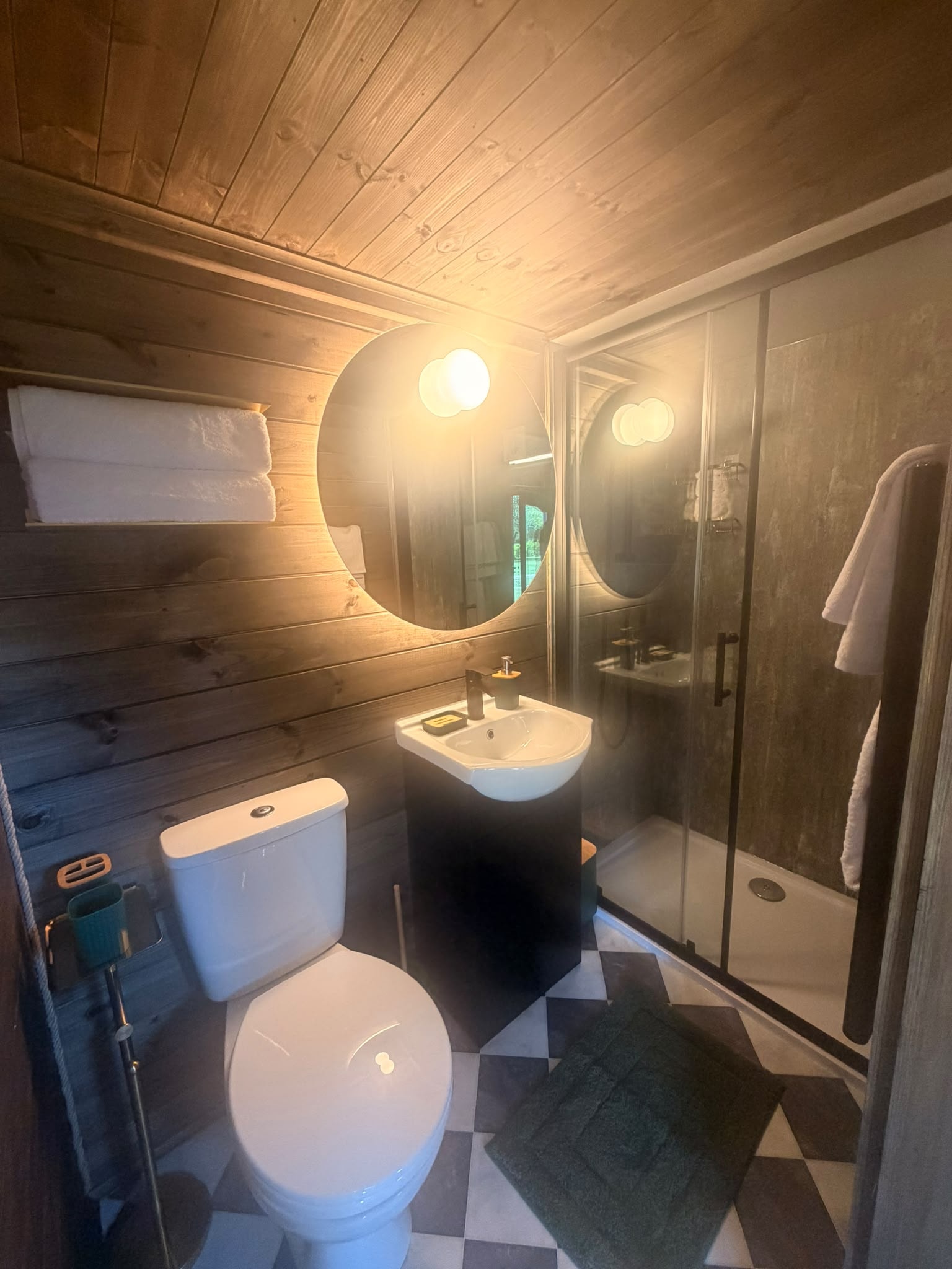 Elmtree Cabins bathroom with wood panelling, round mirror and walk-in shower